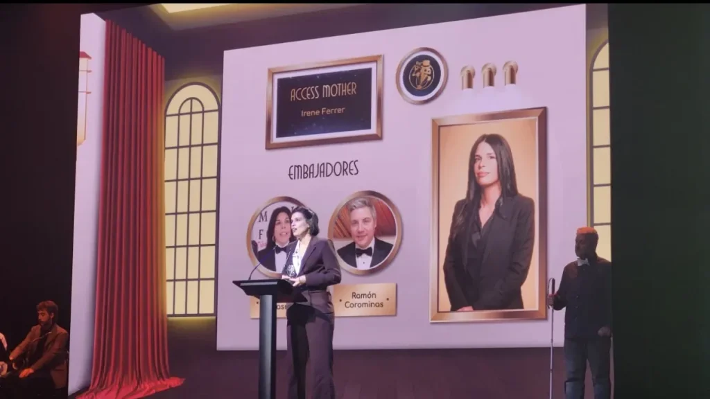 Irene Ferrer en el atril de la Gala de Sirviendo Código 2026, ante la pantalla que la anuncia ganadora del premio Access Mother.